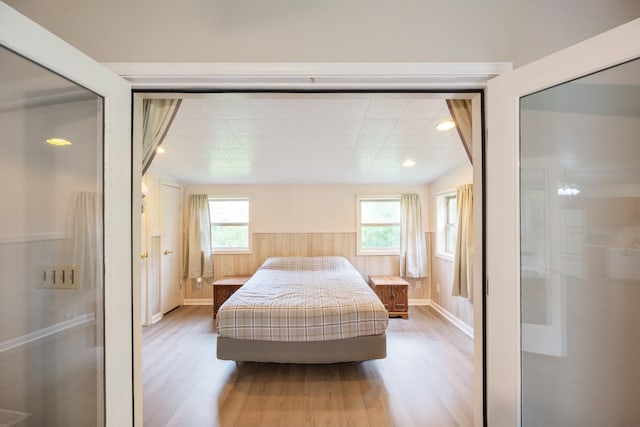 bedroom featuring light wood finished floors, recessed lighting, baseboards, and a wainscoted wall