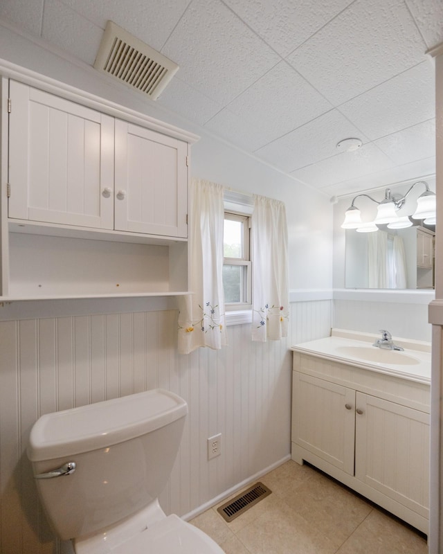 half bath with toilet, wainscoting, vanity, and tile patterned floors