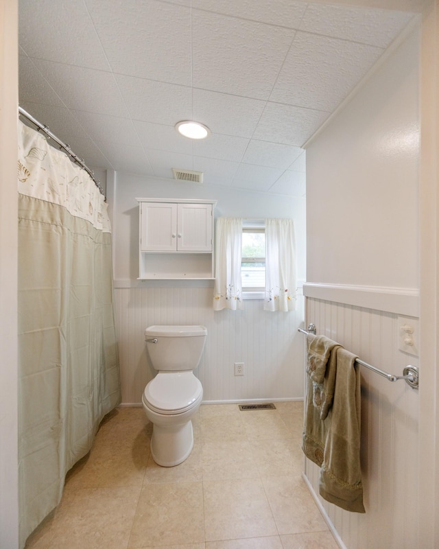 bathroom with wainscoting, tile patterned floors, toilet, a shower with curtain, and a drop ceiling