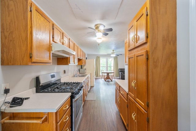 kitchen featuring stainless steel gas range, under cabinet range hood, a ceiling fan, dark wood finished floors, and light countertops