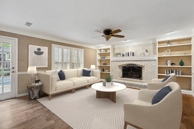living area featuring dark wood finished floors, ceiling fan, ornamental molding, a brick fireplace, and built in features