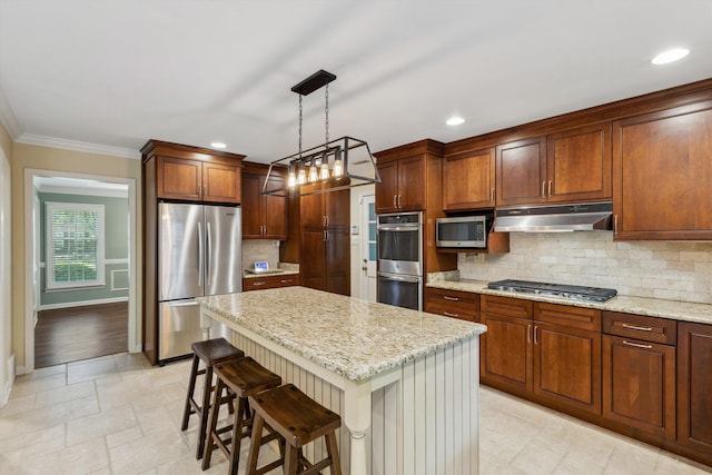 kitchen with stainless steel appliances, under cabinet range hood, a kitchen breakfast bar, light stone countertops, and crown molding