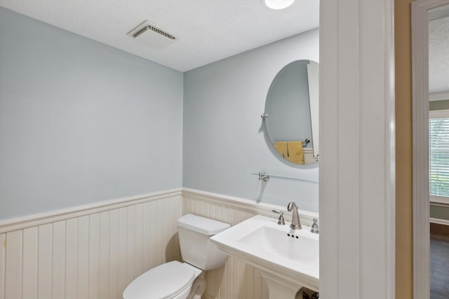 half bath featuring a wainscoted wall, toilet, and a sink