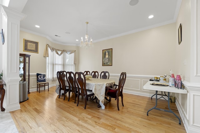 dining space with decorative columns, a decorative wall, light wood-type flooring, a chandelier, and a wainscoted wall
