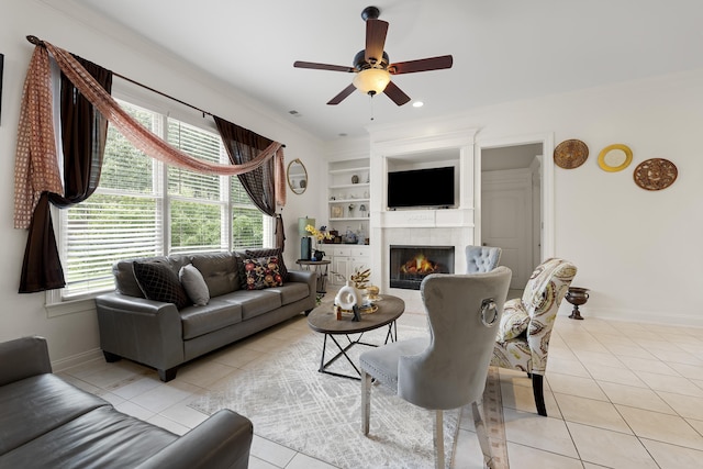 living room featuring light tile patterned floors, baseboards, ceiling fan, a tiled fireplace, and crown molding