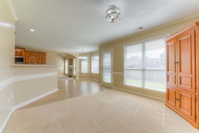 unfurnished living room featuring light carpet, a chandelier, arched walkways, baseboards, and a textured ceiling