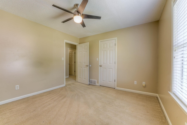 unfurnished bedroom featuring light colored carpet, baseboards, a ceiling fan, and a textured ceiling