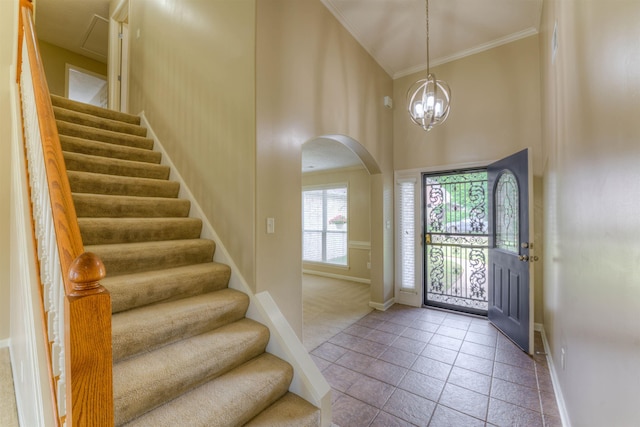 foyer entrance featuring baseboards, arched walkways, crown molding, stairs, and tile patterned flooring