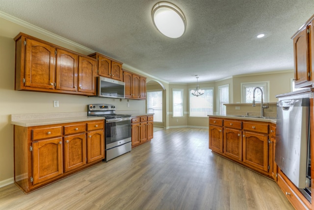 kitchen with stainless steel appliances, a sink, crown molding, a textured ceiling, and arched walkways
