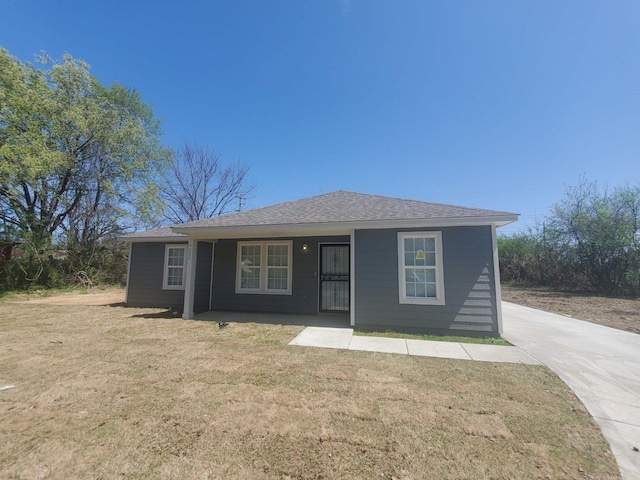 view of front facade with a front yard, roof with shingles, and covered porch