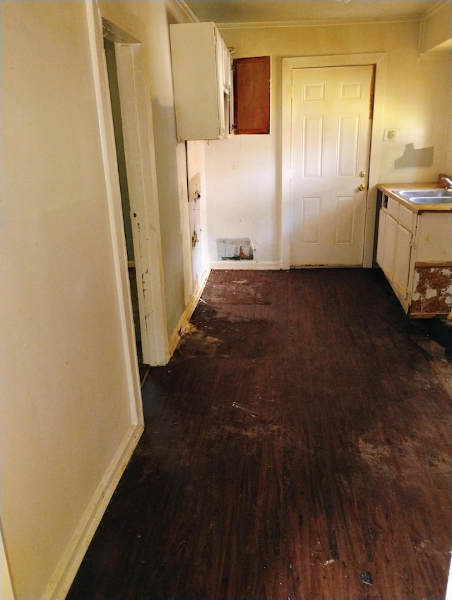 hallway featuring dark wood-type flooring, a sink, baseboards, and crown molding
