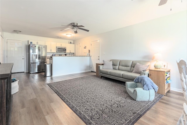 living area with a ceiling fan, wood finished floors, and baseboards