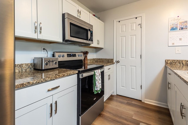 kitchen featuring appliances with stainless steel finishes, dark wood-style flooring, dark stone counters, white cabinets, and baseboards