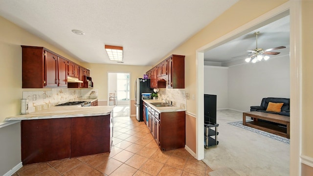 kitchen featuring light countertops, freestanding refrigerator, decorative backsplash, a sink, and under cabinet range hood