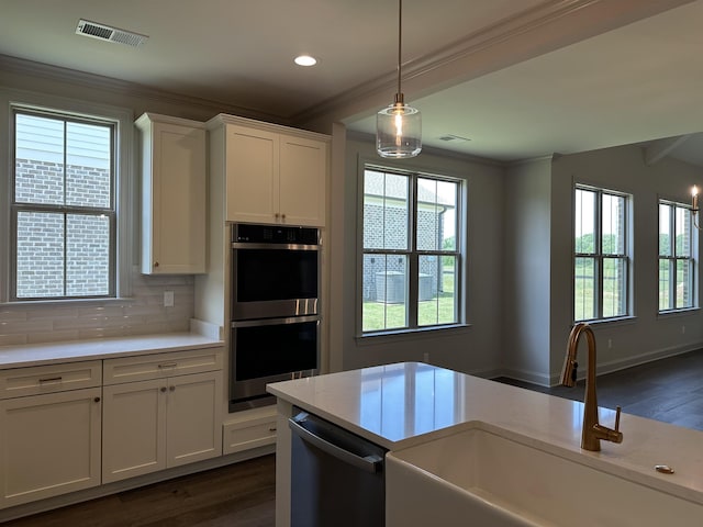kitchen with stainless steel appliances, a sink, light countertops, decorative backsplash, and ornamental molding
