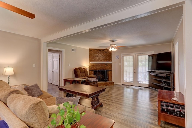 living area with a ceiling fan, wood finished floors, a fireplace, a textured ceiling, and french doors