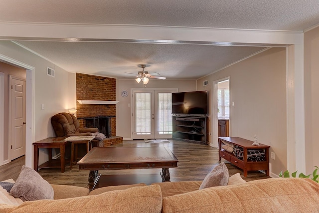 living room with wood finished floors, a fireplace, a ceiling fan, crown molding, and a textured ceiling