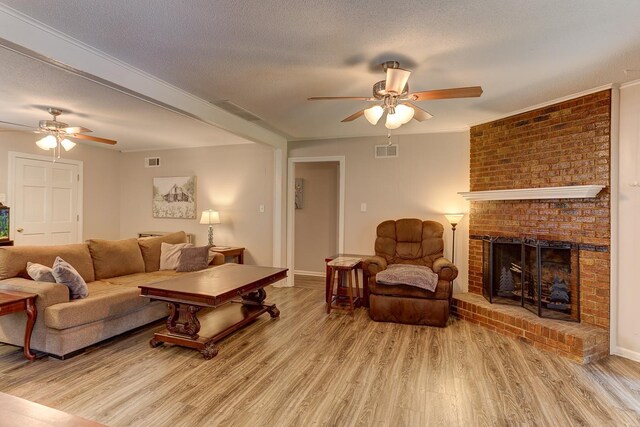 living room featuring ceiling fan, wood finished floors, a brick fireplace, a textured ceiling, and baseboards