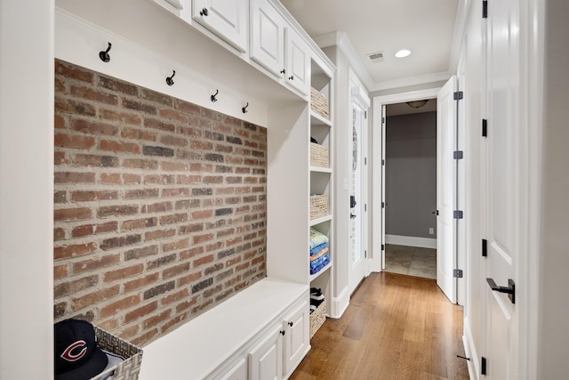 mudroom featuring brick wall, crown molding, and wood finished floors