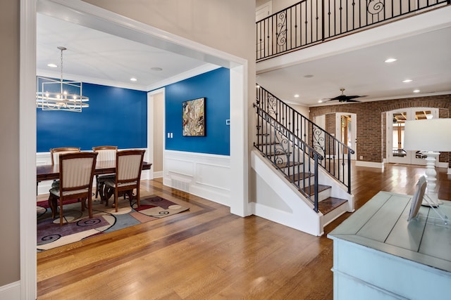 dining room with wood finished floors, stairway, a chandelier, ceiling fan, and brick wall