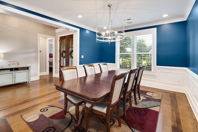 dining room with crown molding, a chandelier, a wainscoted wall, light wood-style flooring, and french doors
