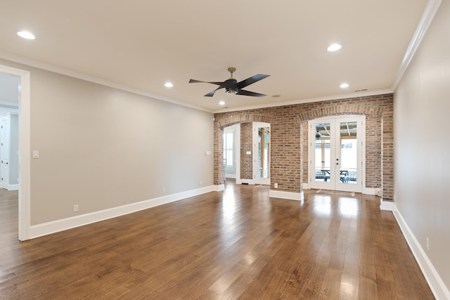unfurnished living room with french doors, brick wall, arched walkways, ceiling fan, and ornamental molding
