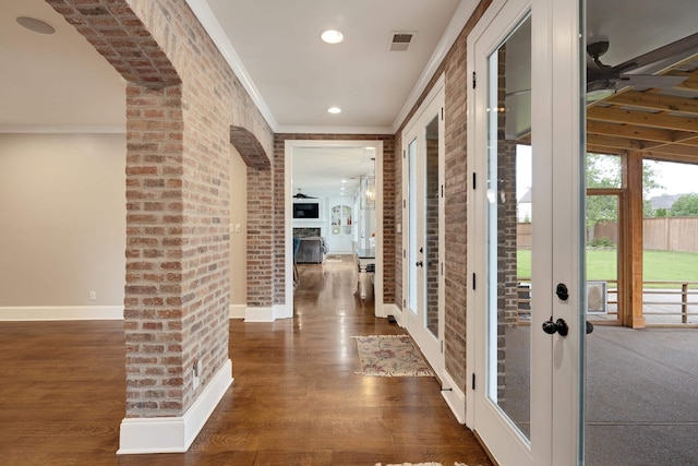 hall featuring wood finished floors, ornamental molding, baseboards, recessed lighting, and brick wall