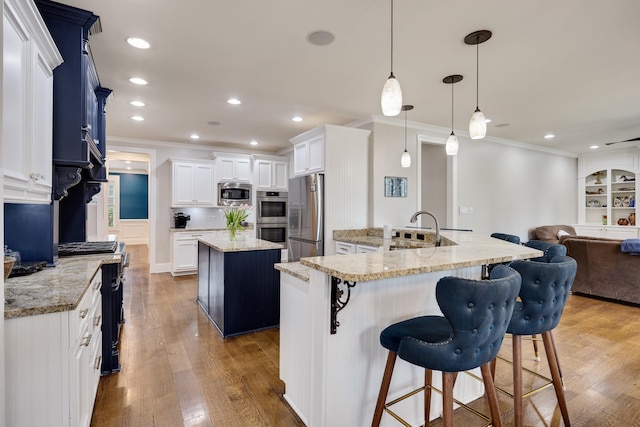 kitchen with appliances with stainless steel finishes, ornamental molding, a sink, open floor plan, and a kitchen breakfast bar