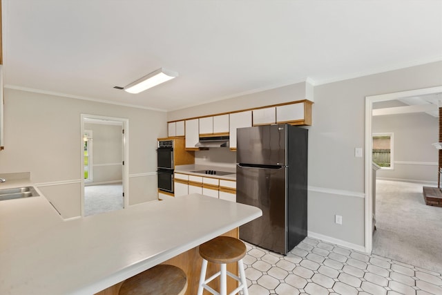 kitchen with black appliances, light countertops, a peninsula, under cabinet range hood, and ornamental molding