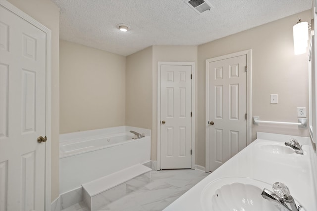 bathroom with marble finish floors, a bath, a textured ceiling, and double vanity