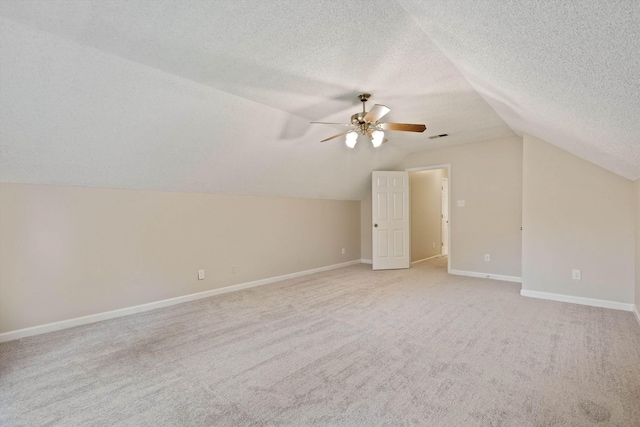 additional living space with a ceiling fan, vaulted ceiling, light colored carpet, a textured ceiling, and baseboards