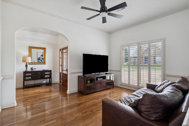 living area with arched walkways, wood finished floors, a ceiling fan, and ornamental molding