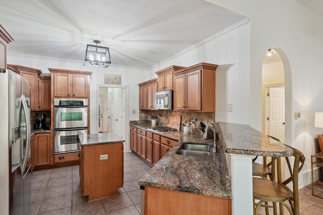 kitchen featuring appliances with stainless steel finishes, a sink, a peninsula, decorative backsplash, and a center island