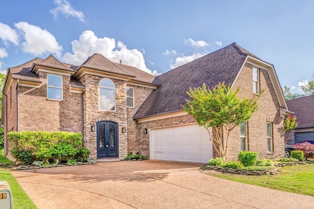 view of front of property featuring concrete driveway, brick siding, an attached garage, french doors, and roof with shingles