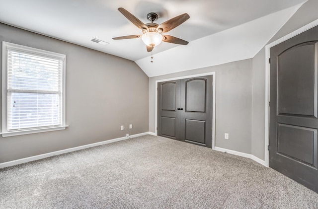unfurnished bedroom featuring carpet floors, vaulted ceiling, baseboards, a closet, and ceiling fan