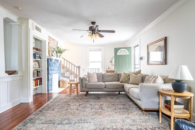living area featuring wood finished floors, built in features, a ceiling fan, crown molding, and a textured ceiling