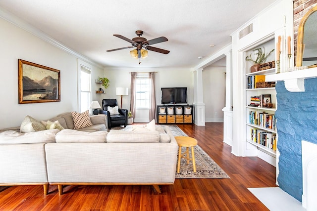 living room featuring ceiling fan, ornamental molding, wood finished floors, ornate columns, and built in features
