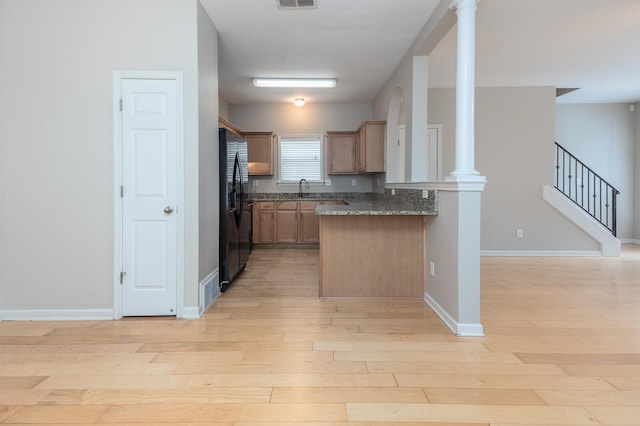 kitchen with light wood finished floors, freestanding refrigerator, a peninsula, ornate columns, and dark stone countertops