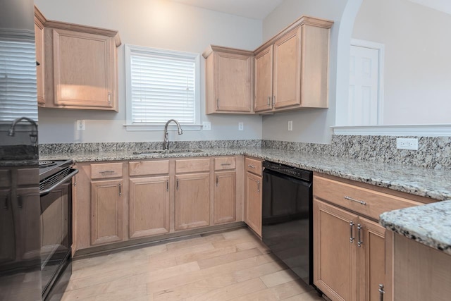 kitchen with black appliances, a sink, light stone counters, light wood-style flooring, and arched walkways