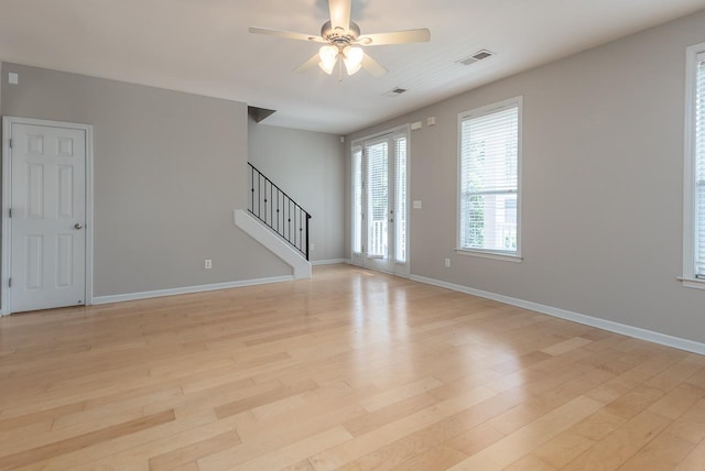 unfurnished room with stairs, light wood-type flooring, a ceiling fan, and baseboards