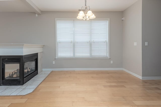 unfurnished living room with light wood finished floors, a chandelier, a tiled fireplace, and healthy amount of natural light