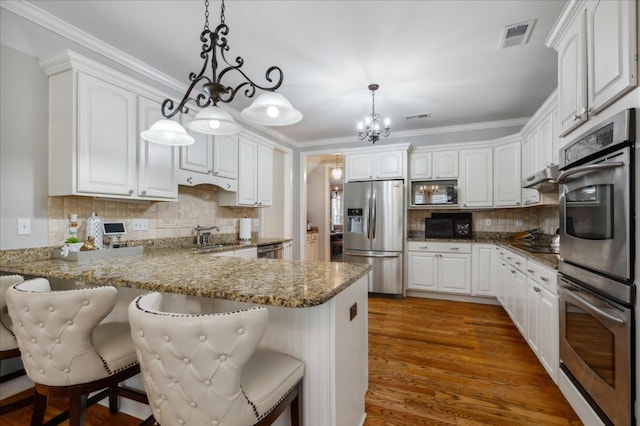 215 Ivy Grove Ln, Collierville, TN 38017 - kitchen featuring stainless steel appliances, a peninsula, white cabinetry, ornamental molding, and under cabinet range hood