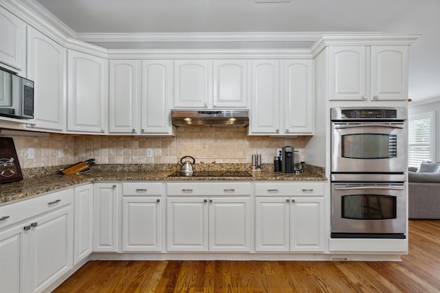 215 Ivy Grove Ln, Collierville, TN 38017 - kitchen featuring under cabinet range hood, appliances with stainless steel finishes, dark stone counters, light wood finished floors, and white cabinets
