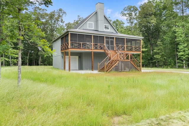 back of house featuring a sunroom, a chimney, stairway, and an attached garage