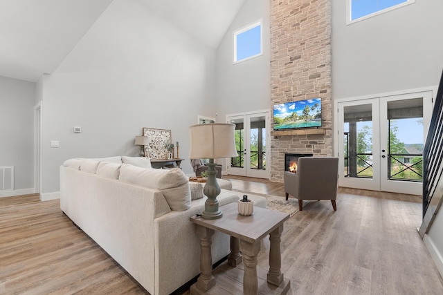 living room featuring high vaulted ceiling, french doors, light wood-style flooring, a fireplace, and baseboards