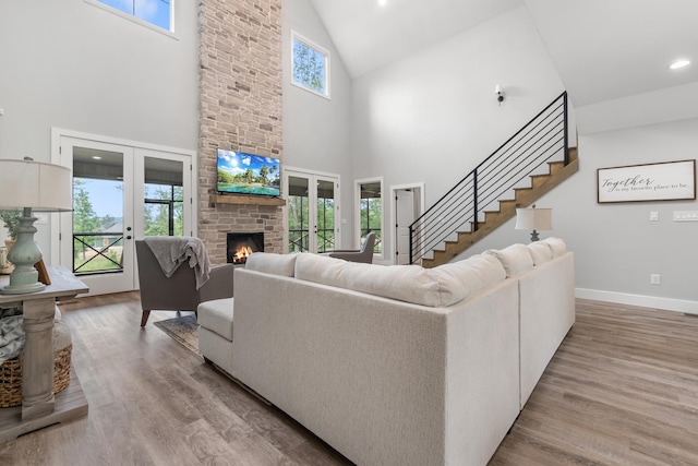 living area with french doors, high vaulted ceiling, a stone fireplace, wood finished floors, and recessed lighting