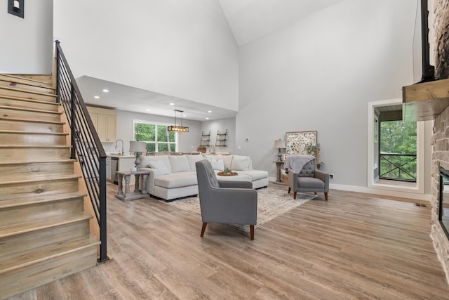 living room featuring stairs, a fireplace, high vaulted ceiling, light wood-style floors, and baseboards