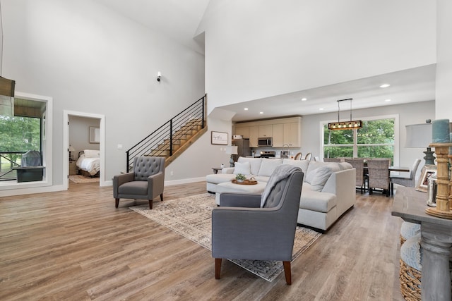 living area with stairway, a high ceiling, light wood finished floors, recessed lighting, and baseboards