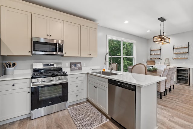 kitchen featuring stainless steel appliances, a sink, wine cooler, a peninsula, and light countertops