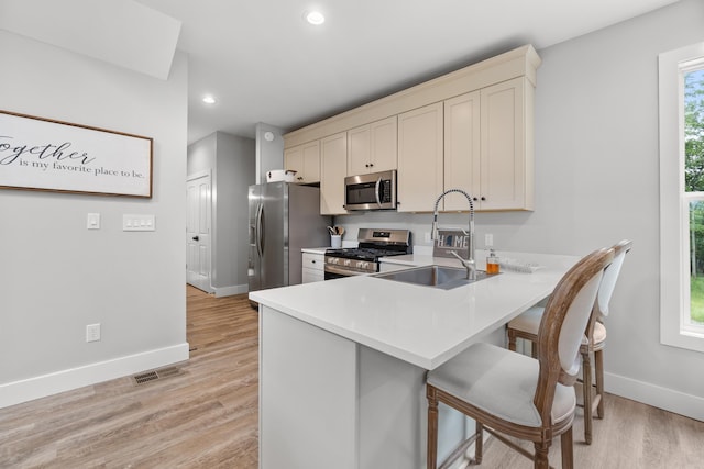 kitchen with stainless steel appliances, a sink, baseboards, a kitchen breakfast bar, and recessed lighting